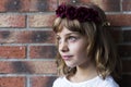 Portrait of a beautiful little girl wearing a red wreath roses on her head. Brick background. Lifestyle Royalty Free Stock Photo