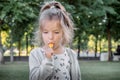 Portrait of beautiful little girl 4-7 years old with lollipop in summer park on natural background