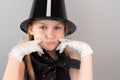 Portrait of beautiful little sad blonde girl in hat and gloves depicting smile sitting at table on gray background Royalty Free Stock Photo