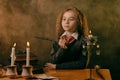 Little witch dressed in dark clothes sitting at the table against a black smoky background. There are magic wand, books Royalty Free Stock Photo
