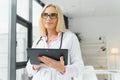 Portrait of beautiful mature woman doctor holding digital tablet. Confident female doctor using digital tablet with Royalty Free Stock Photo