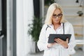 Portrait of beautiful mature woman doctor holding digital tablet. Confident female doctor using digital tablet with Royalty Free Stock Photo