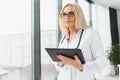 Portrait of beautiful mature woman doctor holding digital tablet. Confident female doctor using digital tablet with Royalty Free Stock Photo