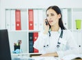 Beautiful medical doctor talking on the phone looking at laptop screen in the office. Royalty Free Stock Photo