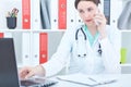 Portrait of a beautiful medical doctor talking on the phone looking at the laptop screen. Royalty Free Stock Photo