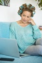 Portrait of beautiful middle age adult woman work and use laptop computer at home sitting onthe sofa with curlers in the hair for Royalty Free Stock Photo