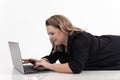Portrait of beautiful middle-aged fat plus-size woman wearing black cardigan, lying on white floor, typing on laptop.