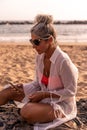 Portrait of beautiful middle aged woman relaxing using phone sitting at the beach Royalty Free Stock Photo