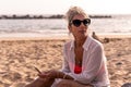 Portrait of beautiful middle aged woman relaxing using phone sitting at the beach Royalty Free Stock Photo