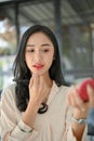 Portrait of a beautiful millennial Asian woman applying red lipstick, putting on her makeup Royalty Free Stock Photo