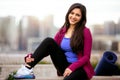 Portrait of a beautiful mixed ethnicity brunette woman in sportswear, sitting relaxed after a morning yoga workout with city skyli