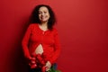 Beautiful curly haired brunette, pregnant woman holding bouquet of red tulips, smiling a toothy smile, looking at camera Royalty Free Stock Photo