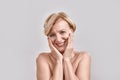 Portrait of beautiful naked middle aged woman looking excited, smiling at camera, touching her cheeks while posing Royalty Free Stock Photo