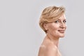 Portrait of beautiful naked middle aged woman smiling at camera while posing  against grey background. Beauty Royalty Free Stock Photo