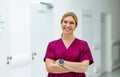 Portrait of beautiful nurse in uniform, standing in the hospital corridor with arms crossed, looking at the camera and Royalty Free Stock Photo