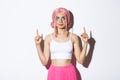 Portrait of beautiful party girl with pink wig and glamour makeup, pointing fingers and looking up, showing your logo Royalty Free Stock Photo