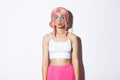 Portrait of beautiful party girl with pink wig and halloween makeup, pouting silly, standing over white background Royalty Free Stock Photo