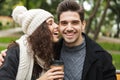 Portrait of beautiful people man and woman 20s laughing and drinking takeaway coffee from paper cups, while sitting on bench in Royalty Free Stock Photo