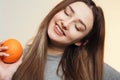 Portrait of a beautiful positive girl with long hair and orange, a young woman smiling and holding fruit near face on studio Royalty Free Stock Photo