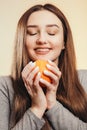Portrait of a beautiful positive girl with long hair and orange, a young woman smiling and holding fruit near face on studio Royalty Free Stock Photo