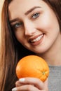 Portrait of a beautiful positive girl with long hair and orange, a young woman smiling and holding fruit near face on studio Royalty Free Stock Photo