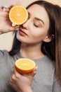 Portrait of a beautiful positive girl with long hair and orange, a young woman smiling and holding fruit near face on studio Royalty Free Stock Photo