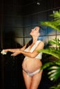 Portrait of beautiful pregnant girl in white underwear washes in the shower, covered with soap foam. Close-up