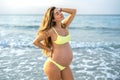 Portrait of beautiful pregnant woman in yellow swimsuit posing on the beach. Royalty Free Stock Photo