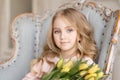 Portrait of beautiful pretty girl with yellow flowers tulips sitting in arm-chair, smiling. Indoor photo. Spring theme. Close-up Royalty Free Stock Photo