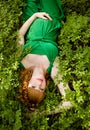 portrait of a beautiful red-haired pregnant girl in a green dress, lying in the grass