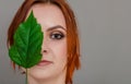 Portrait of a beautiful red-haired woman, half of her face closed by a large green leaf of a Chinese rose. Women`s health, natura Royalty Free Stock Photo