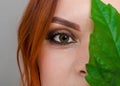 Portrait of a beautiful red-haired woman, half of her face closed by a large green leaf of a Chinese rose. Women`s health, natura Royalty Free Stock Photo