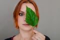 Portrait of a beautiful red-haired woman, half of her face closed by a large green leaf of a Chinese rose. Women`s health, natura Royalty Free Stock Photo