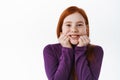 Portrait of beautiful redhead child, little ginger girl with freckles touch cheeks and smiling happy at camera, look Royalty Free Stock Photo