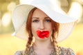 Portrait of beautiful redhead woman in white hat on green field with poppy flower in her mouth Royalty Free Stock Photo