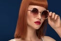 Beautiful redhead girl in sunglasses on blue background. Royalty Free Stock Photo