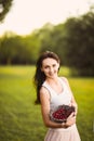 Portrait of a beautiful romantic brunette girl with a basket of cherries in a green garden