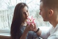 beautiful romantic young couple man woman in love sitting by window looking at each other holding pink red lily flower Royalty Free Stock Photo