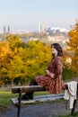 Portrait of beautiful romantic young woman sitting on bench in park, autumn in Prague, yellow brown golden leaves, cute stylish Royalty Free Stock Photo