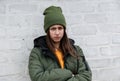 Portrait of a beautiful sad girl in a yellow sweater and khaki hat, which stands near a white brick wall. The concept of emotions Royalty Free Stock Photo