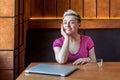 Portrait of beautiful satisfied happy young bussineswoman with blonde short hair in pink t-shirt is sitting in cafe, finishing