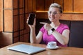 Portrait of beautiful satisfied happy young bussineswoman with blonde short hair in pink t-shirt is sitting in cafe, holding phone