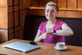 Portrait of beautiful satisfied happy young bussineswoman with blonde short hair in pink t-shirt is sitting in cafe, pointing