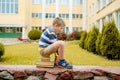 Portrait of Beautiful school boy looking very happy outdoors at the day time. Sitting on the steps with books and a large school Royalty Free Stock Photo