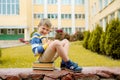 Portrait of Beautiful school boy looking very happy outdoors at the day time. Sitting on the steps with books and a large school Royalty Free Stock Photo