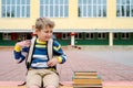 Portrait of Beautiful school boy looking very happy outdoors at the day time. Sitting on the steps with books and a large school Royalty Free Stock Photo