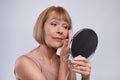 Portrait of beautiful senior woman looking in miror, checking her wrinkles over light studio background Royalty Free Stock Photo