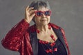 Portrait of beautiful senior woman in red sunglasses and sequin jacket posing in studio