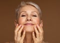 Closeup face of mature woman with wrinkles massaging face isolated over brown background. Aging process concept. Royalty Free Stock Photo