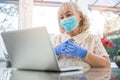 Portrait of beautiful senior woman wearing protective mask and gloves having video chat on laptop at home. Royalty Free Stock Photo